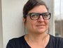 Frau in dunklem T-Shirt lächelt vor heller Balkonwand in die Kamera